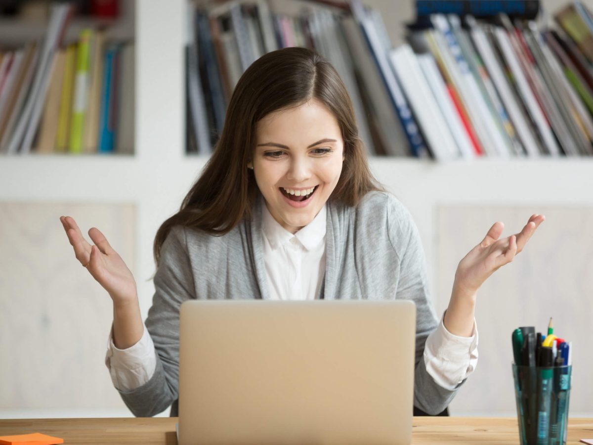 Happy young business woman looking at laptop computer screen in office