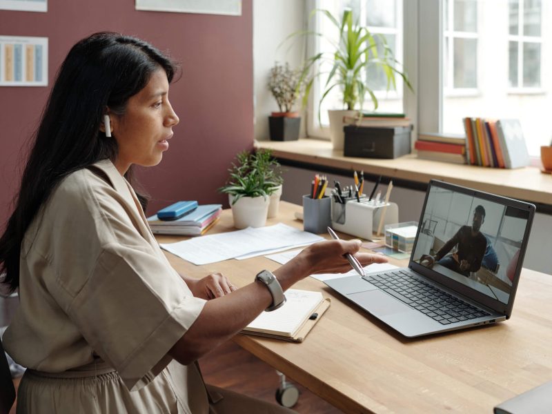 Young woman with earphones speaking to man on laptop screen