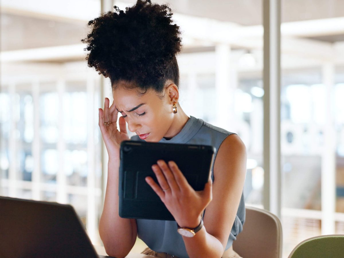 In a modern office space, a young woman sits at a sleek desk, her brow furrowed in concentration as she navigates through her digital tablet.