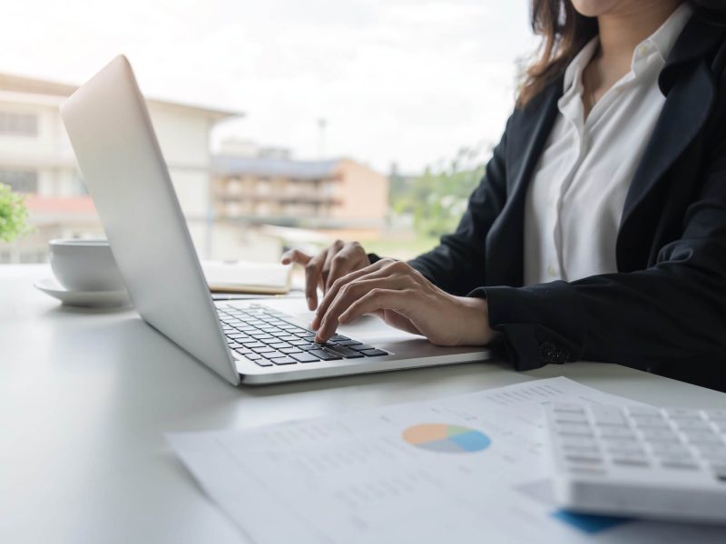 A focused professional working diligently at her laptop, balancing a busy schedule with a fresh cup of coffee and documents spread out, embodying the hustle of modern office life.