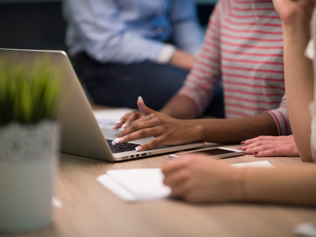 In a collaborative workspace, hands work diligently on a laptop, surrounded by pens and notepads, symbolizing teamwork and creativity. The modern setting captures the essence of productivity as ideas flow and tasks are tackled collectively.